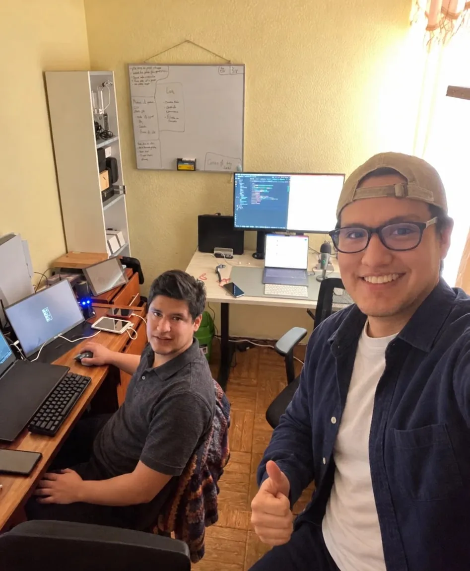 Dos integrantes de Wasilabs en su espacio de trabajo en Lima, frente a sus computadoras y un pizarrón con bocetos.